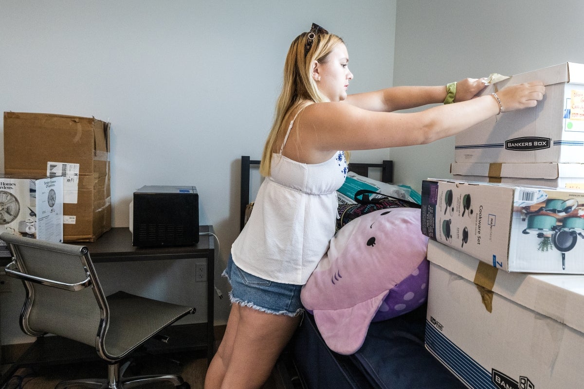 Young woman reaches for a box as she unpacks in her new dorm room