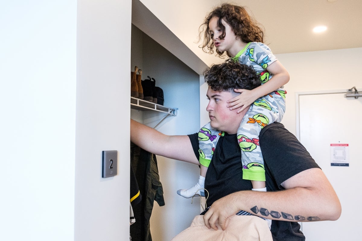 3-year-old kid sitting on the shoulders of his older brother as they unpack in a dorm room