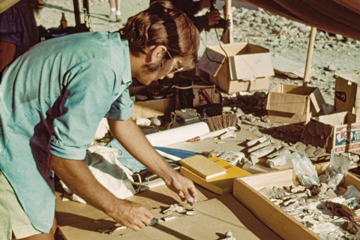 Photo from the 1970s showing a man in a blue shirt surrounded by bone pieces and boxes