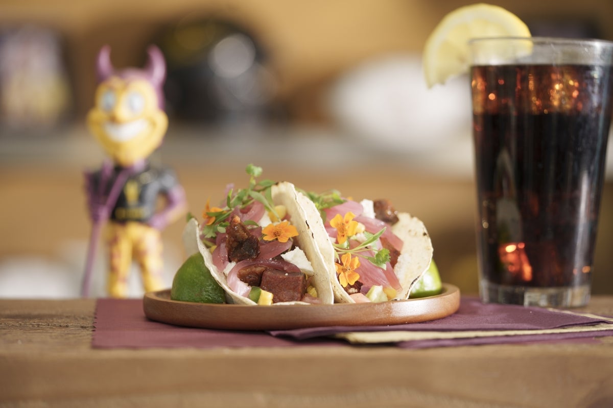 Closeup of two tacos on a table next to a glass of soda