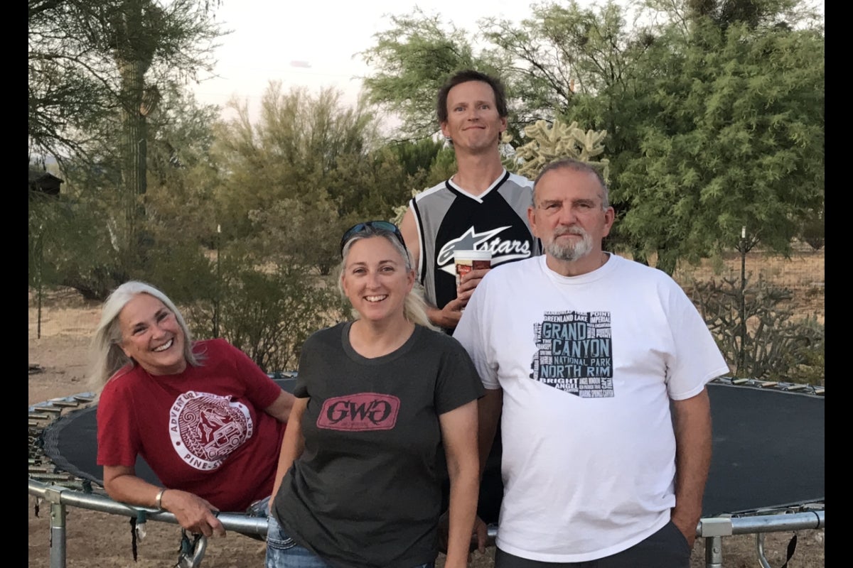 Man, wife and two adult children smiling at the camera in an outdoor setting.