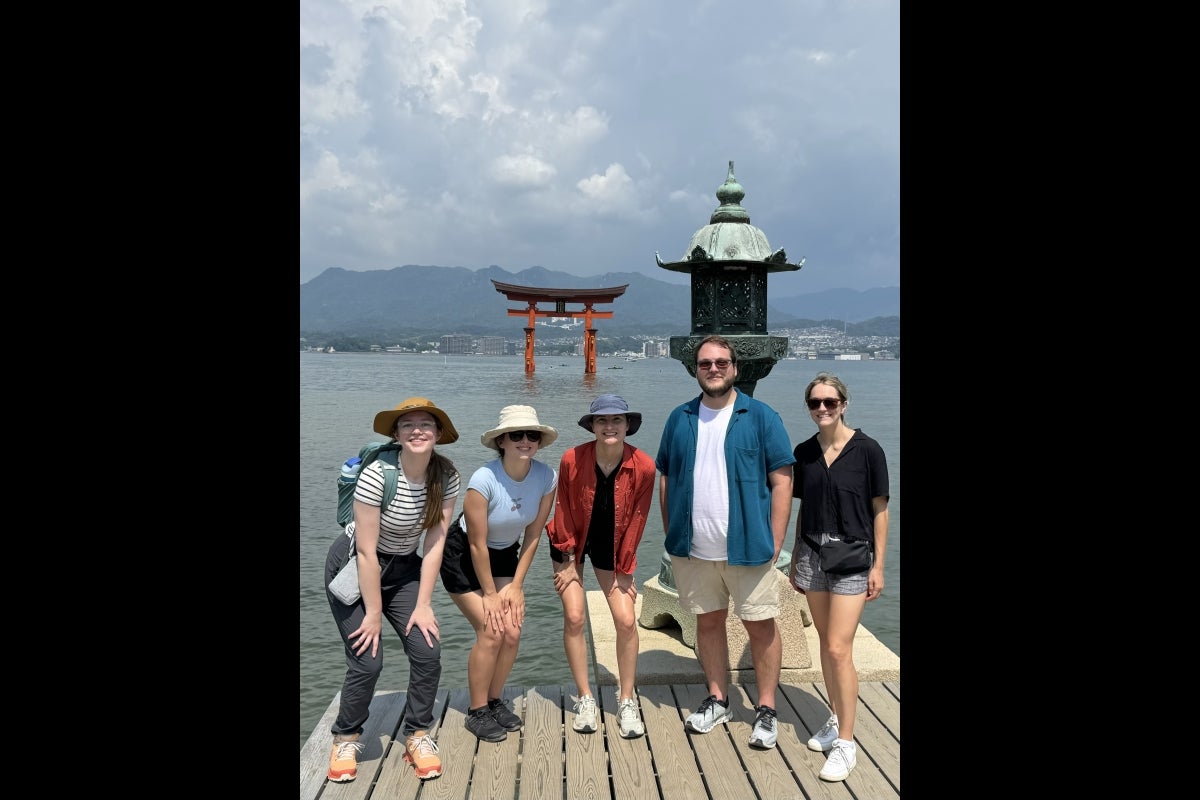 Five people stand posing for a photo on a dock with a body of water behind them