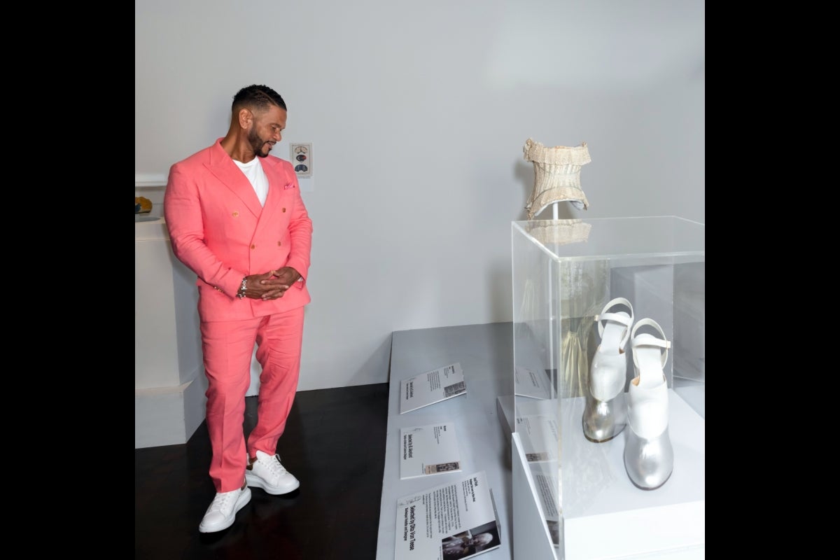 Man in a coral suit observing garments on display in an exhibit.