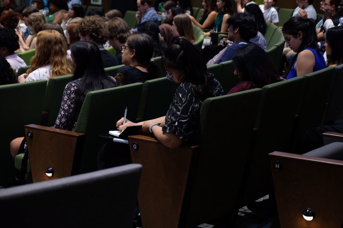 Students seated in an auditorium taking notes and listening to a speaker.