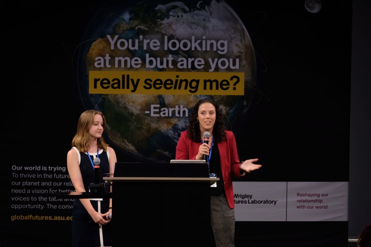 Two women standing behind a lectern as one speaks into a microphone to an unseen audience.