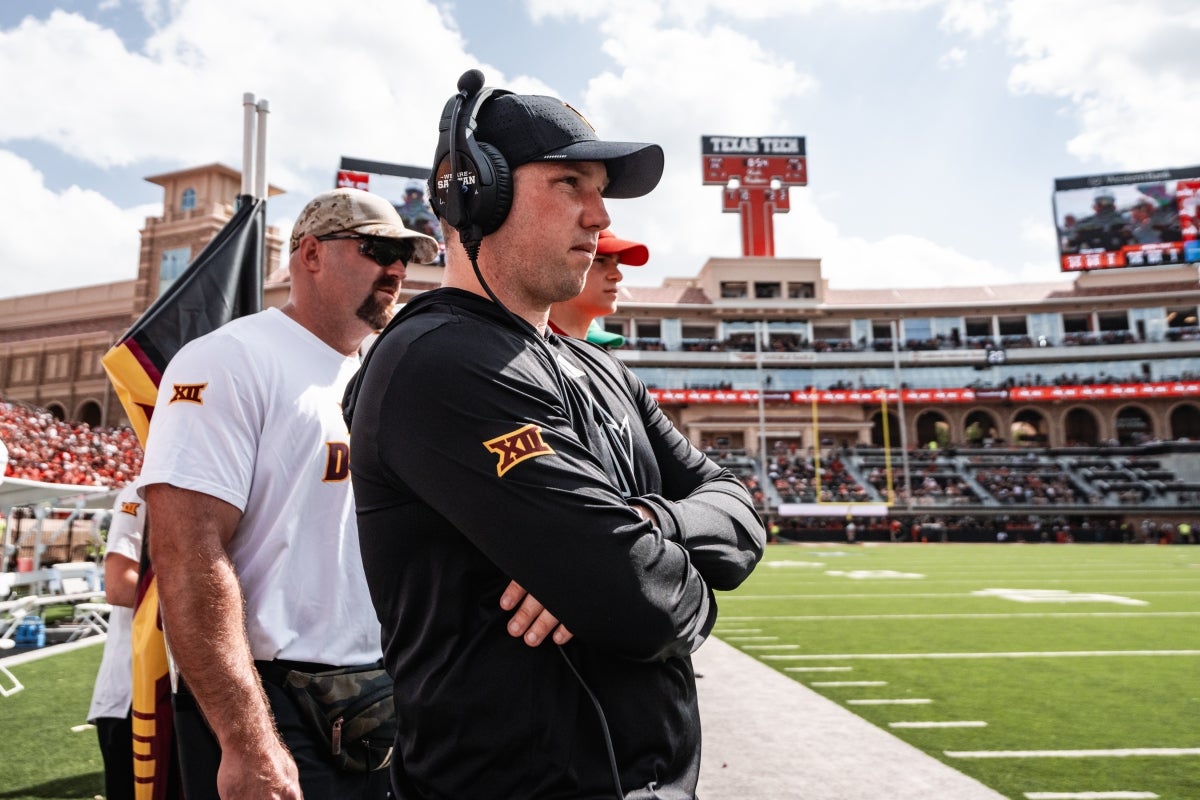 Two coaches watch football game from the sidelines