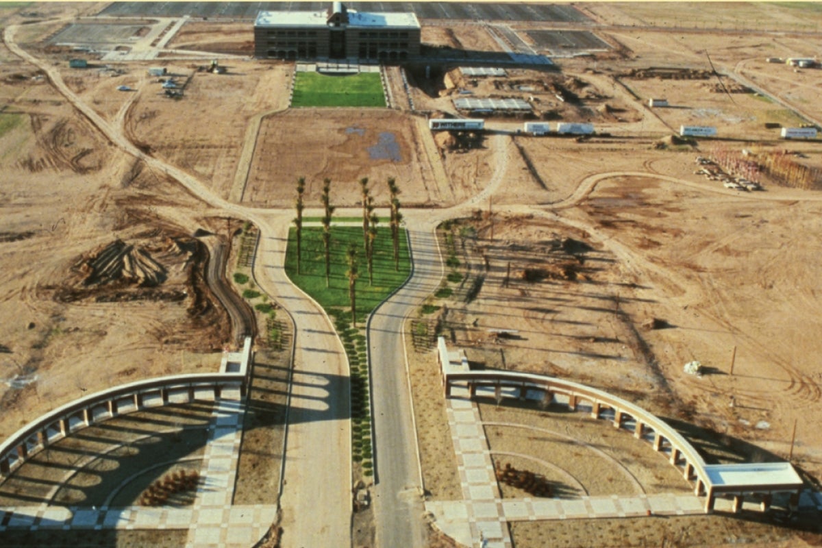 Aerial view of a university campus under construction with dirt and grass and a couple of buildings