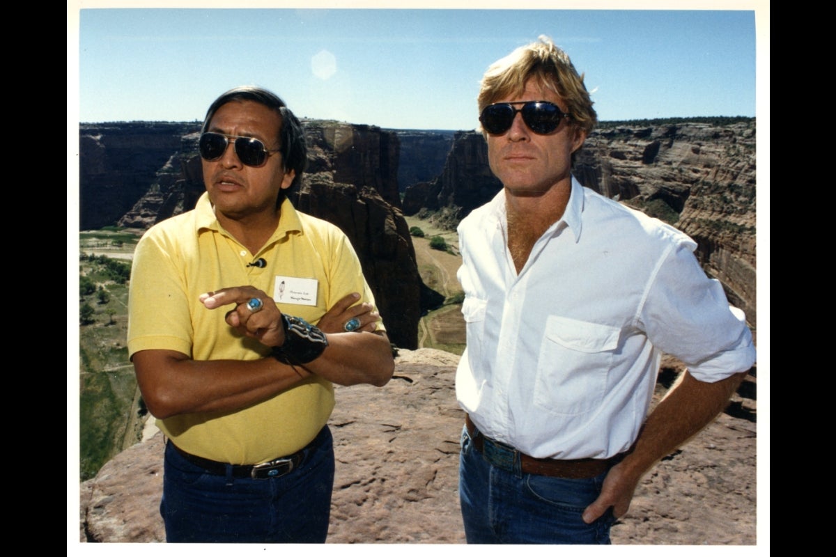 Two men wearing sunglasses stand in a mountainous landscape.