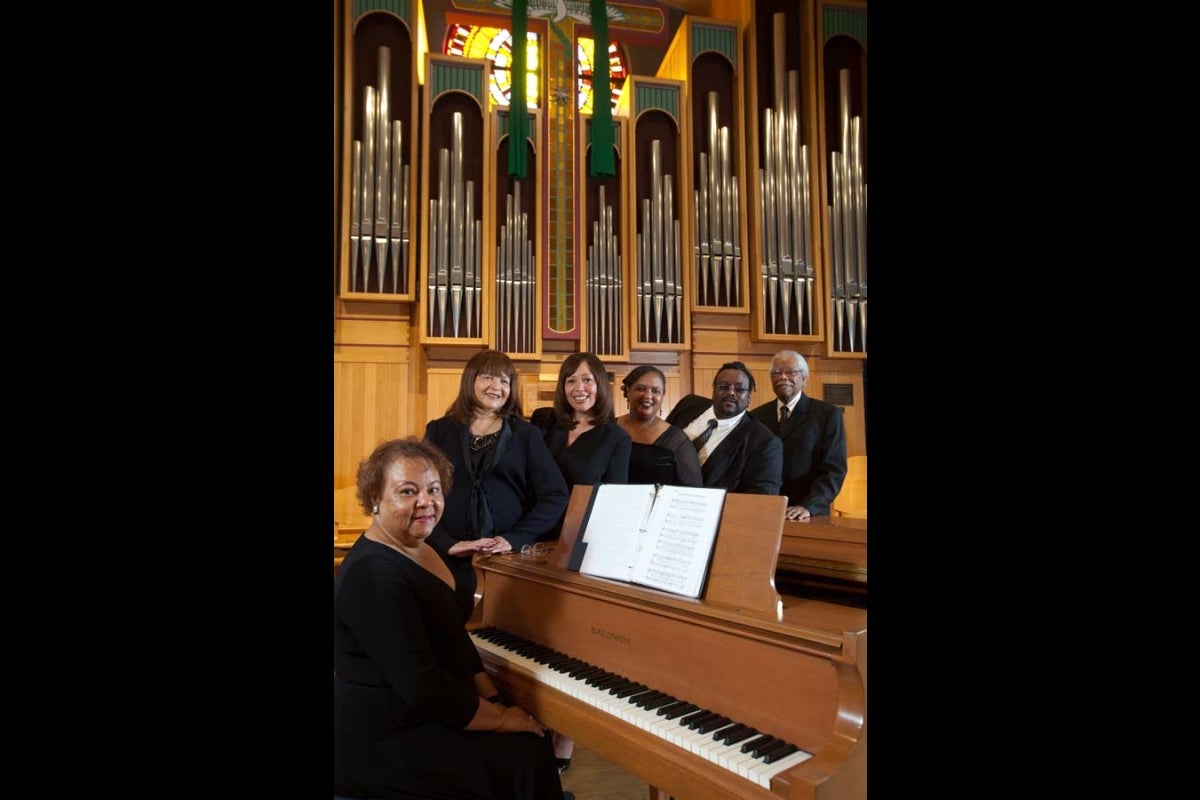 Six people gathered around a piano