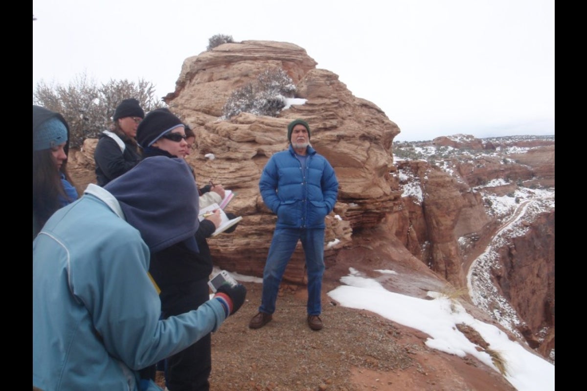 Man standing at the base of a large rock as students take notes.