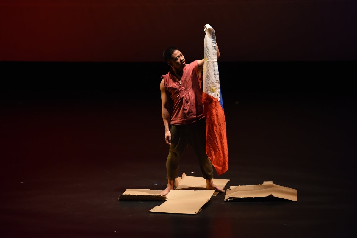 Dancer standing on a stage holding a flag.