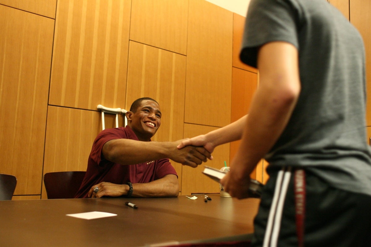 Man at table shakes hands with person greeting him for book signing