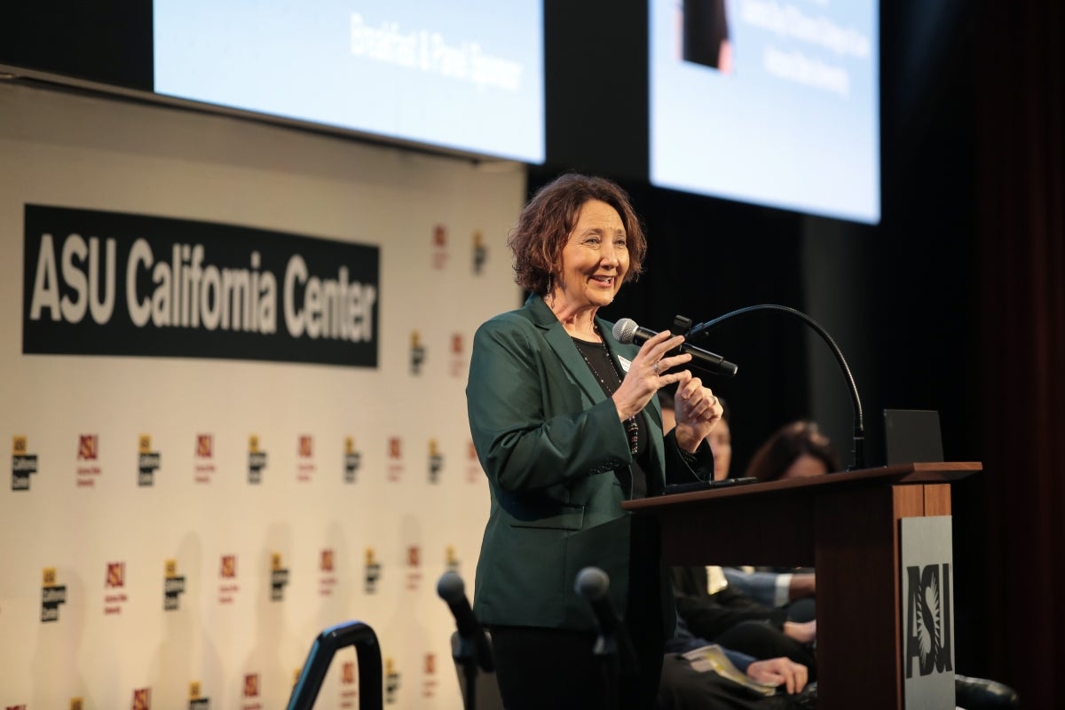 Woman with short brown hair wearing green suit jacket speaks at a lectern