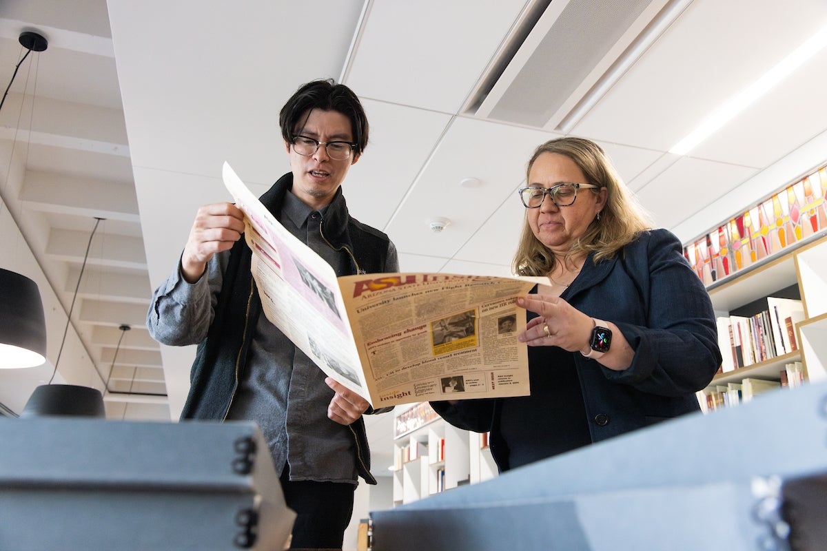 Two people look at a newspaper.