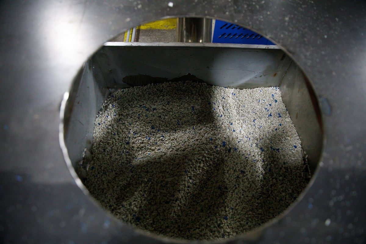 Metal container filled with beige and blue plastic granules seen through a circular opening.