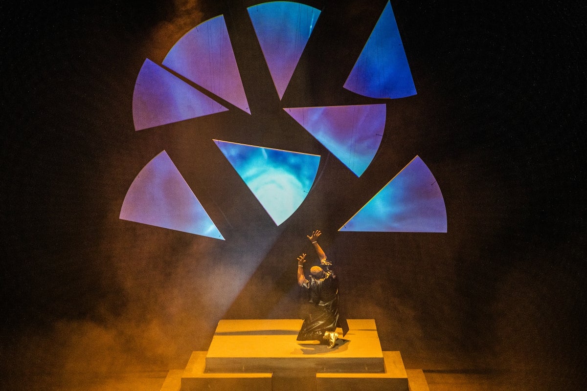 A man performs on stage underneath huge shards of what looks like glass