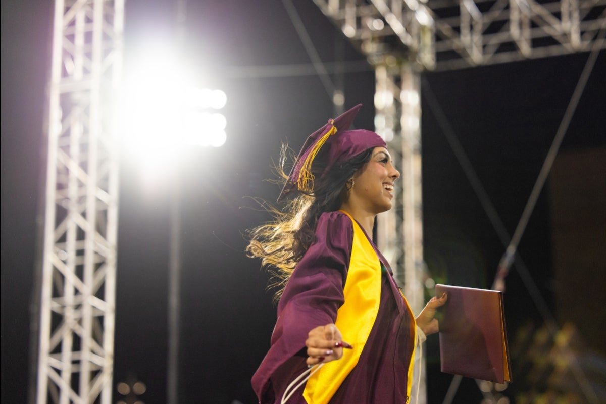 A woman in graduation regalia smiles as she crosses a stage