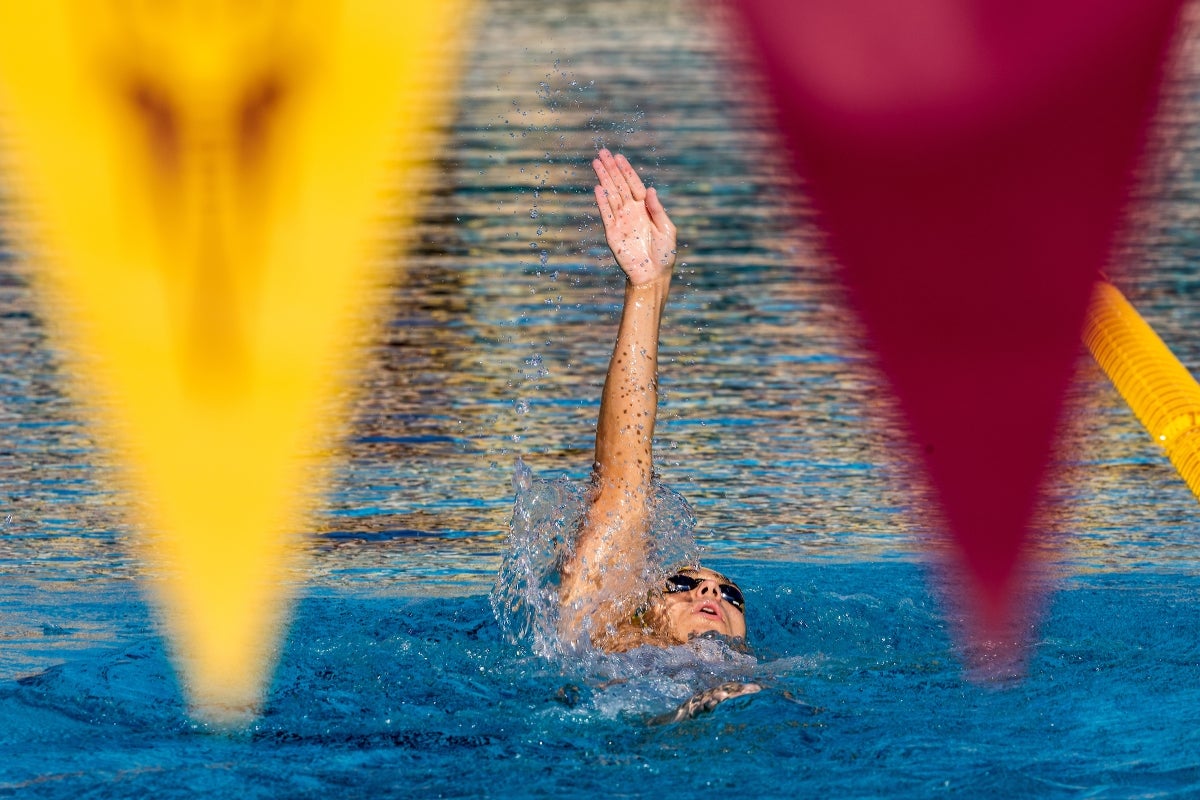 A swimmer doing the backstroke is seen between two pennants hanging on a line