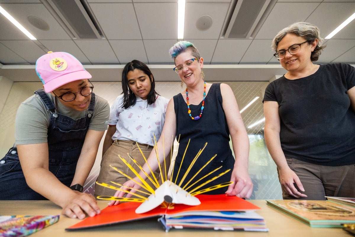 Four people smile as they look at a colorful pop-up book on a table