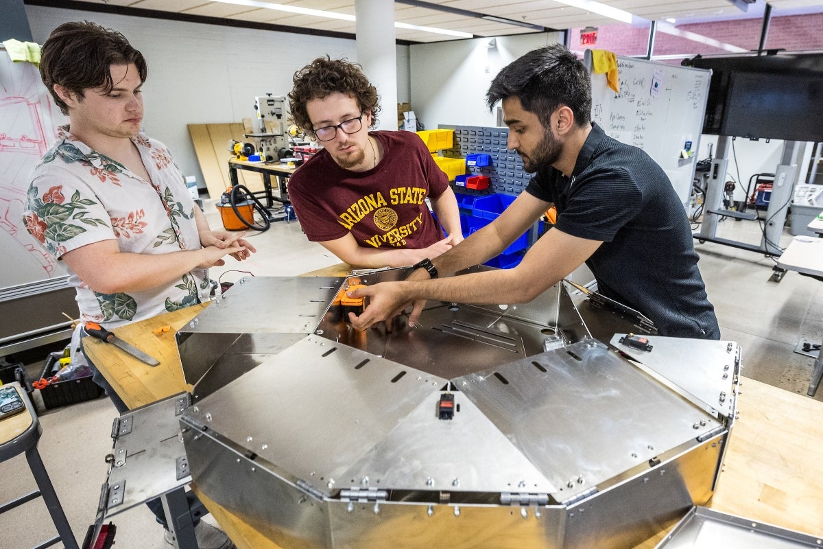 Three young men work on a lunar lander in a lab