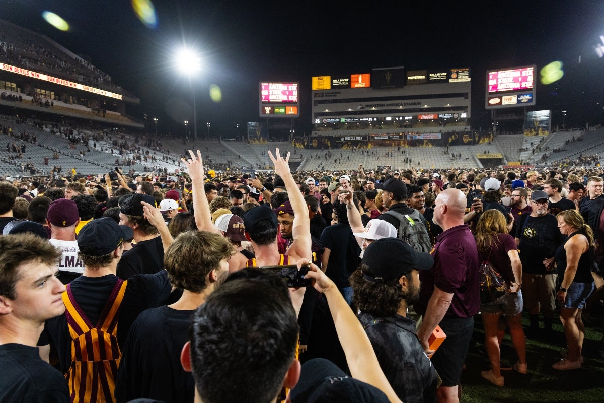 A packed crowd of people crowd onto the field at the ASU football stadium