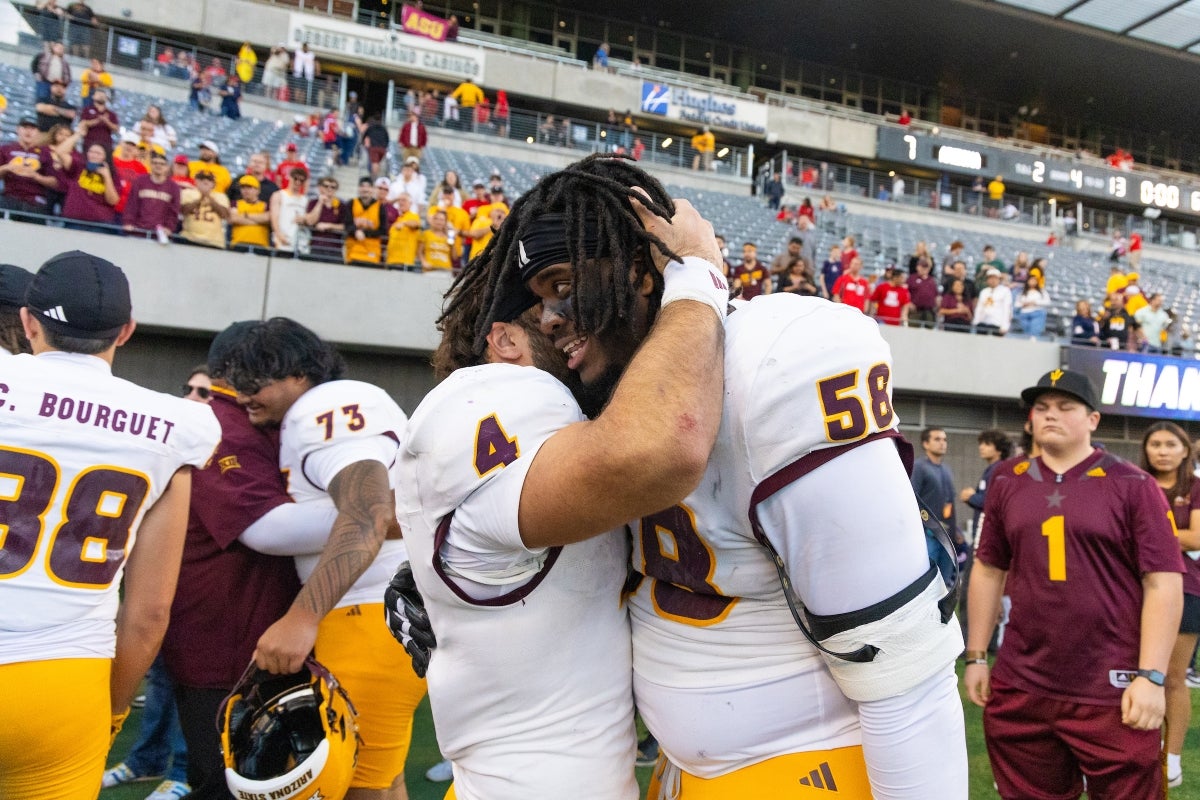 Two ASU football players embrace on field after winning game