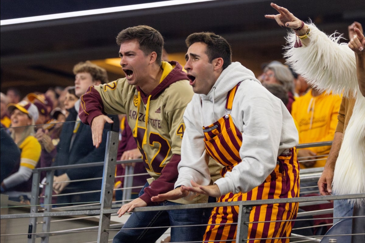 Two ASU fans wearing maroon and gold yell in the football stands