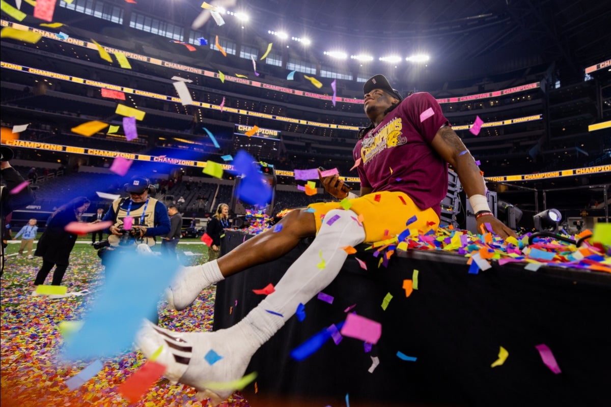 A football player sits on a stage and looks up as confetti falls from the stadium ceiling