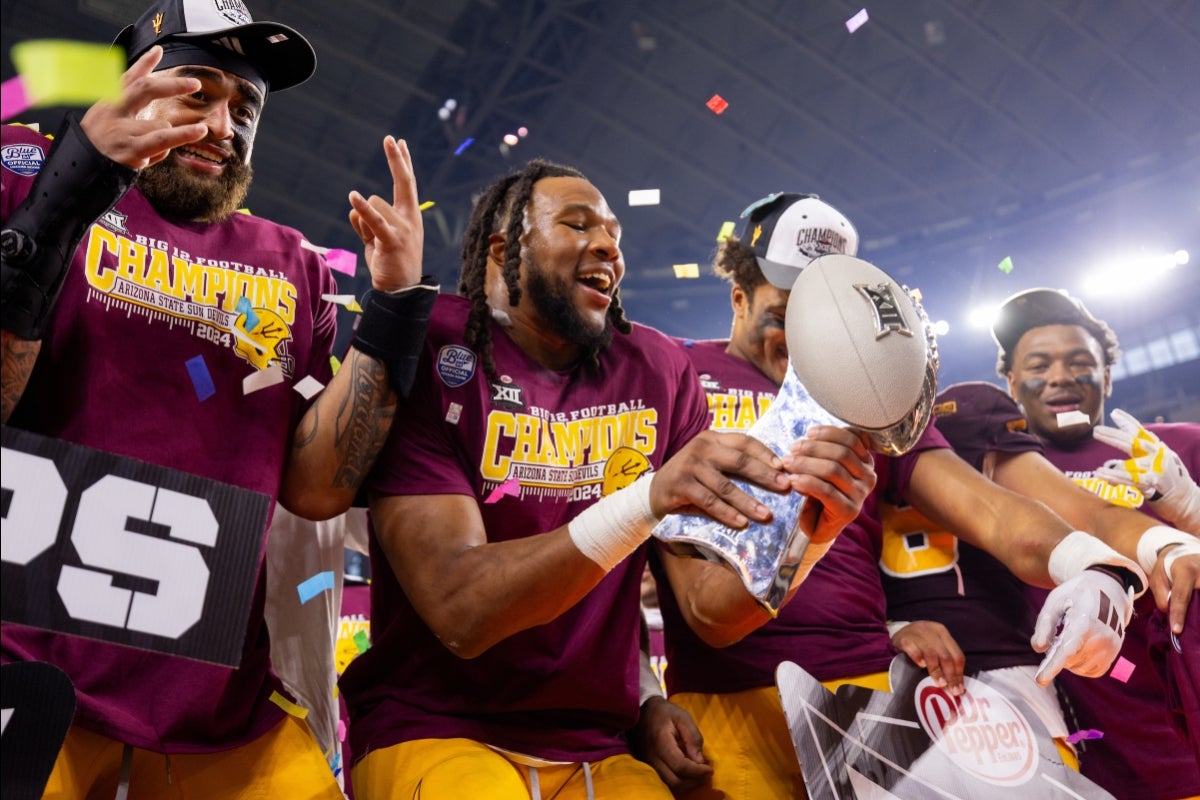 Four ASU football players smile holding the Big 12 football championship trophy