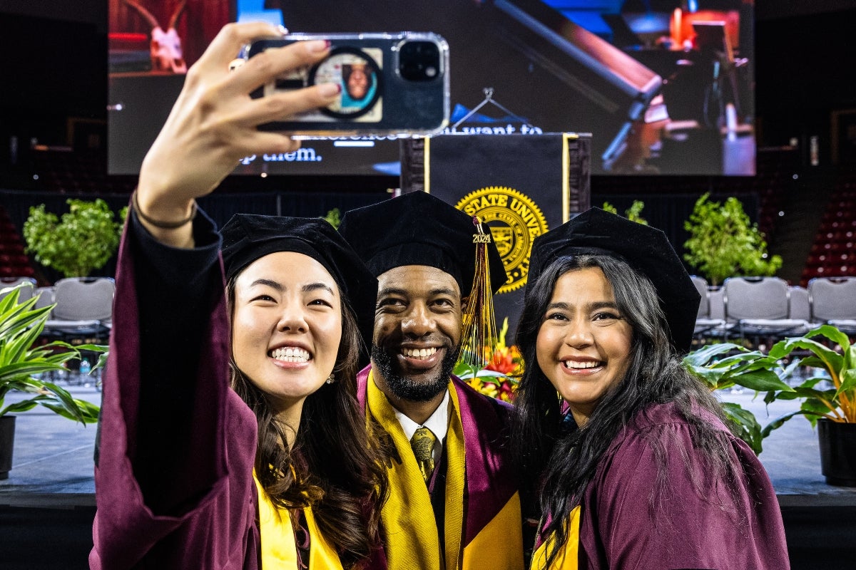 Three graduate students in commencement garb take a selfie