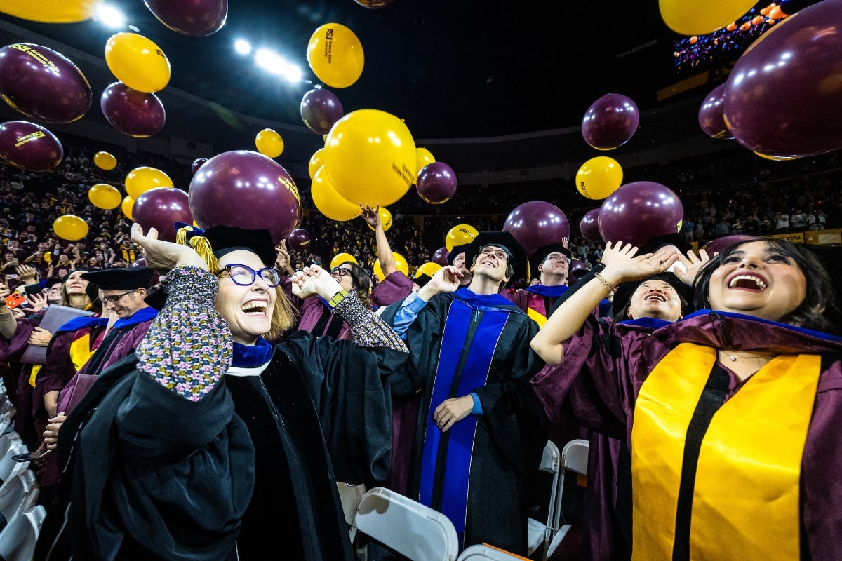 Graduates cheer as large maroon and gold balloons are dropped from the ceiling