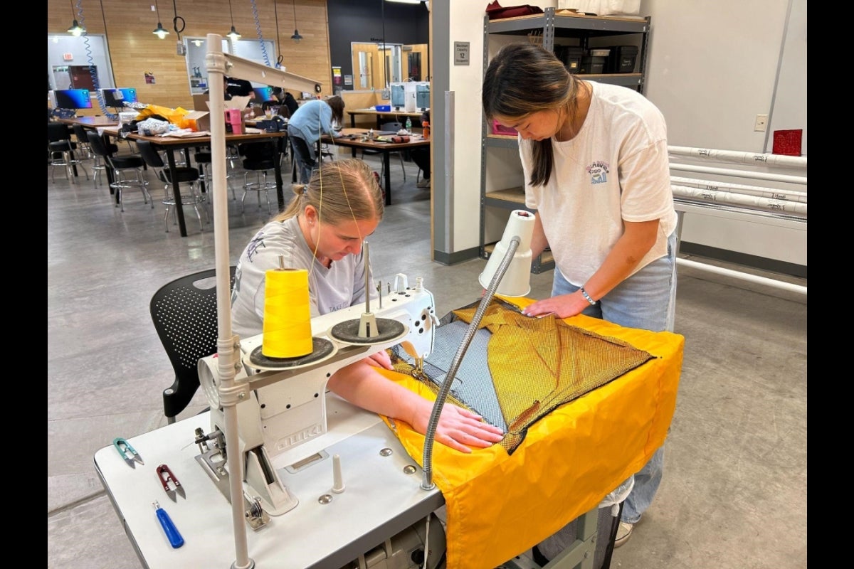 2 young women use a large sewing machine