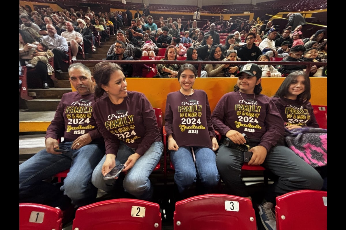 People seated in an arena wearing maroon shirts and smiling.