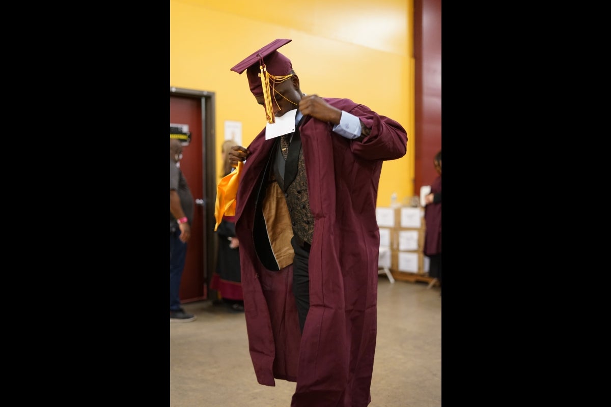 Man in a maroon cap and gown adjusts his gown.