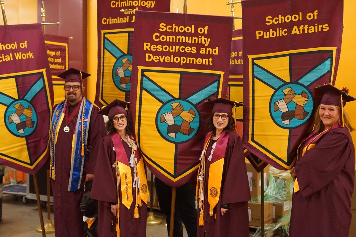 People in maroon graduation caps and gowns hold gonfalons.