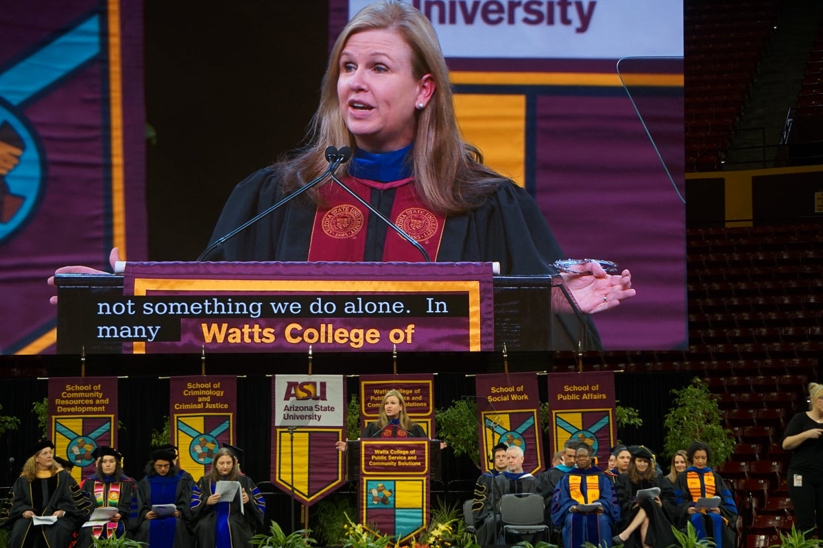 Large screen in an arena displays the face of a college dean as she addresses graduates.