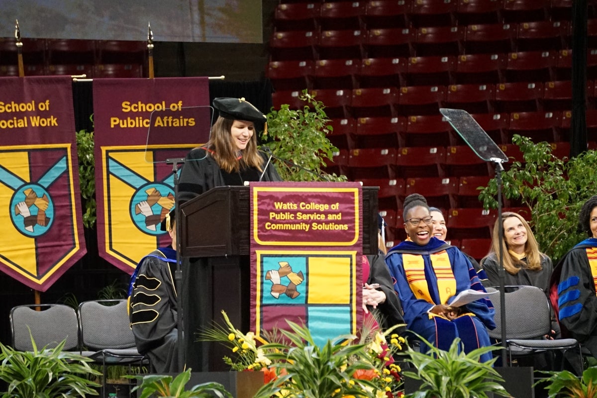 Woman wearing graduation regalia addressing graduates at a ceremony.