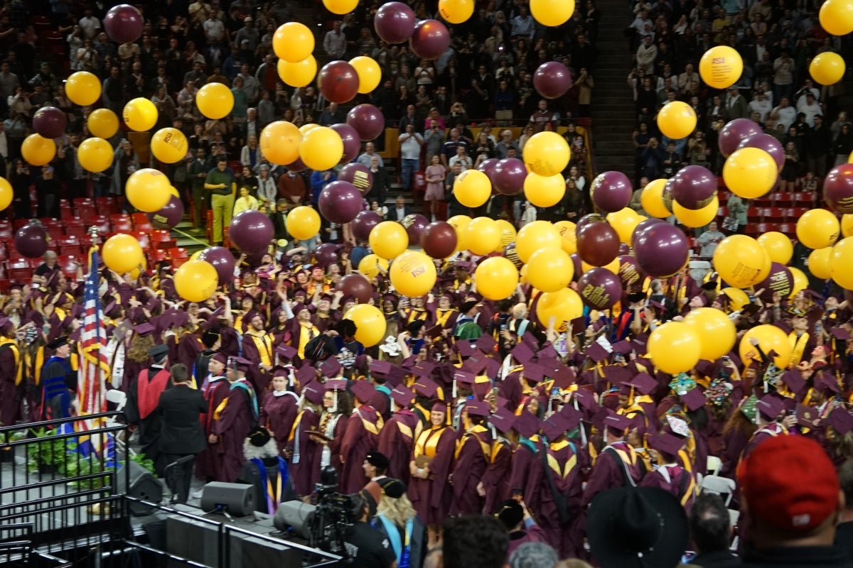 Balloons fall from the ceiling of an arena onto graduates.