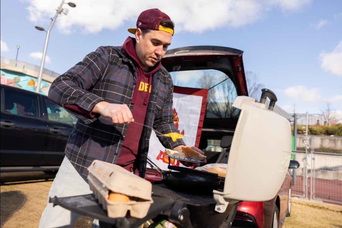 A man in ASU gear makes food on a grill by his truck