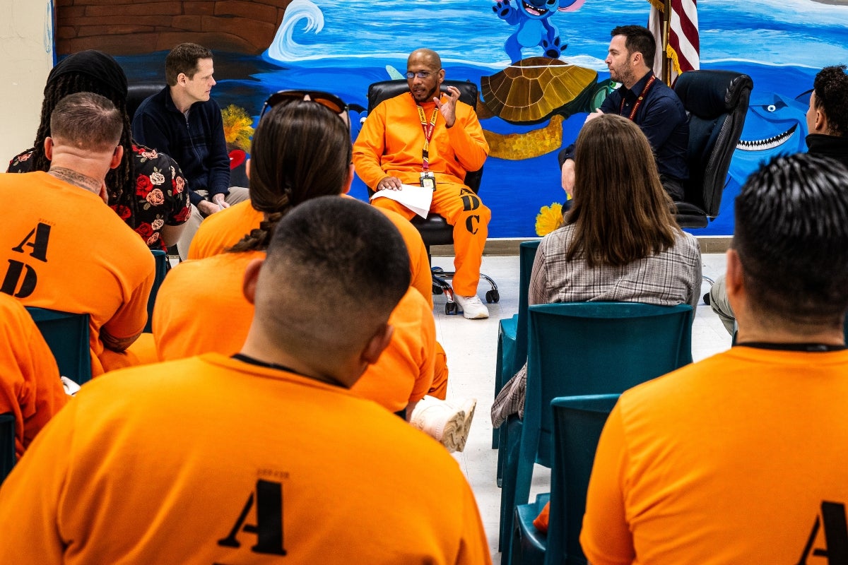 Three people sitting and talking to group of inmates