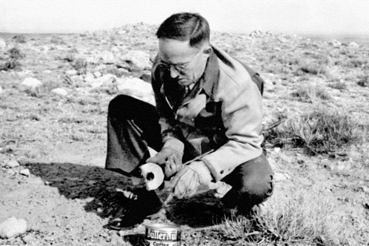 Black and white photo of a man hunched over on the desert ground