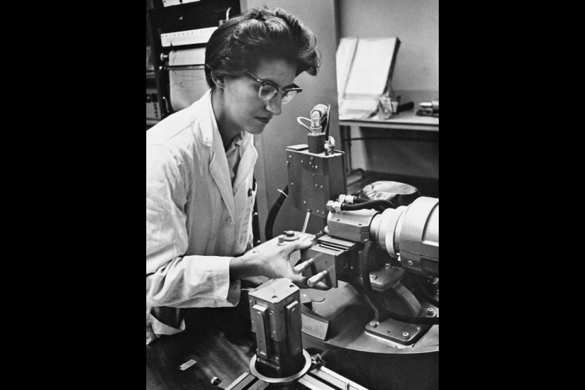 Black and white photo of a woman wearing glasses analyzing meteorites in a lab