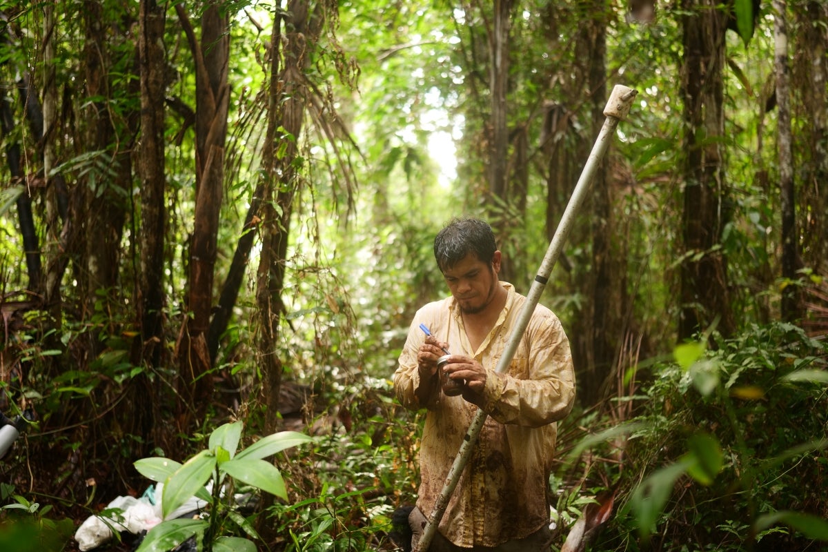 Man holding a jar in a jungle setting.