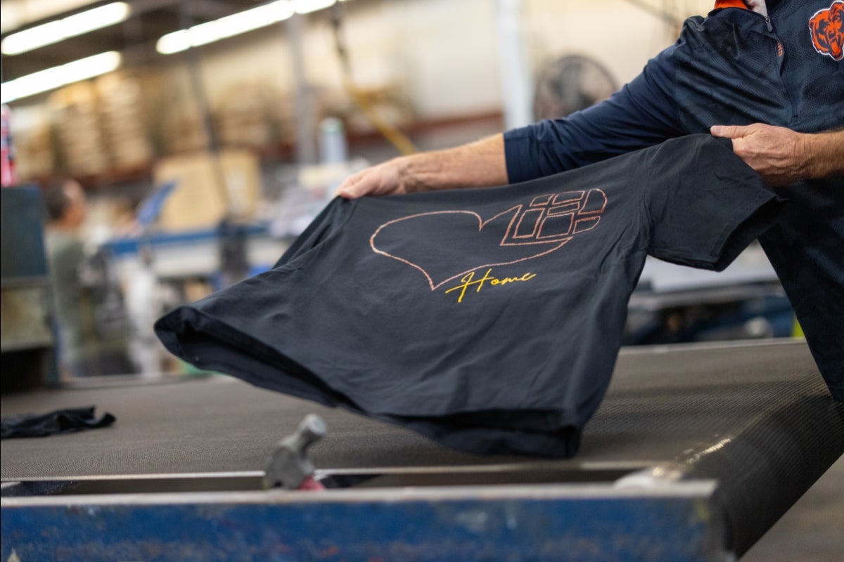 Hands holding a T-shirt with a heart graphic on it.