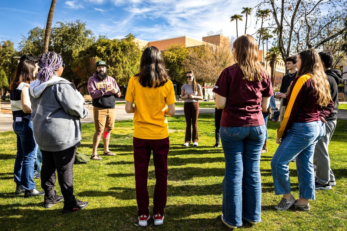 A group of people stands in a circle on a lawn