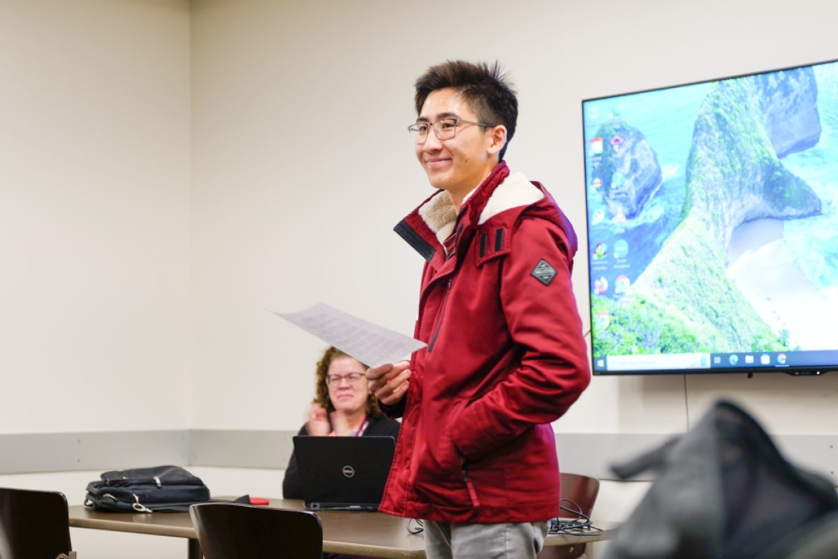 A person wearing a red jacket stands in front of a screen while reading a poem. Photo by Ashley Sorensen/ASU.