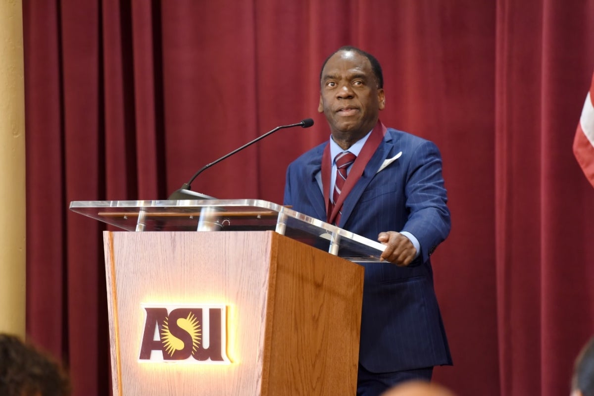 Man speaking into a microphone at a podium to an unseen audience.