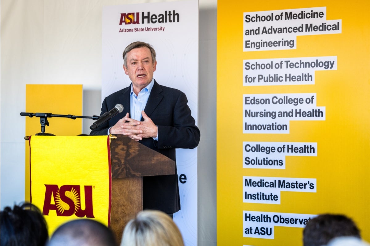 ASU President Michael Crow speaks at a lectern in front of ASU Health signs