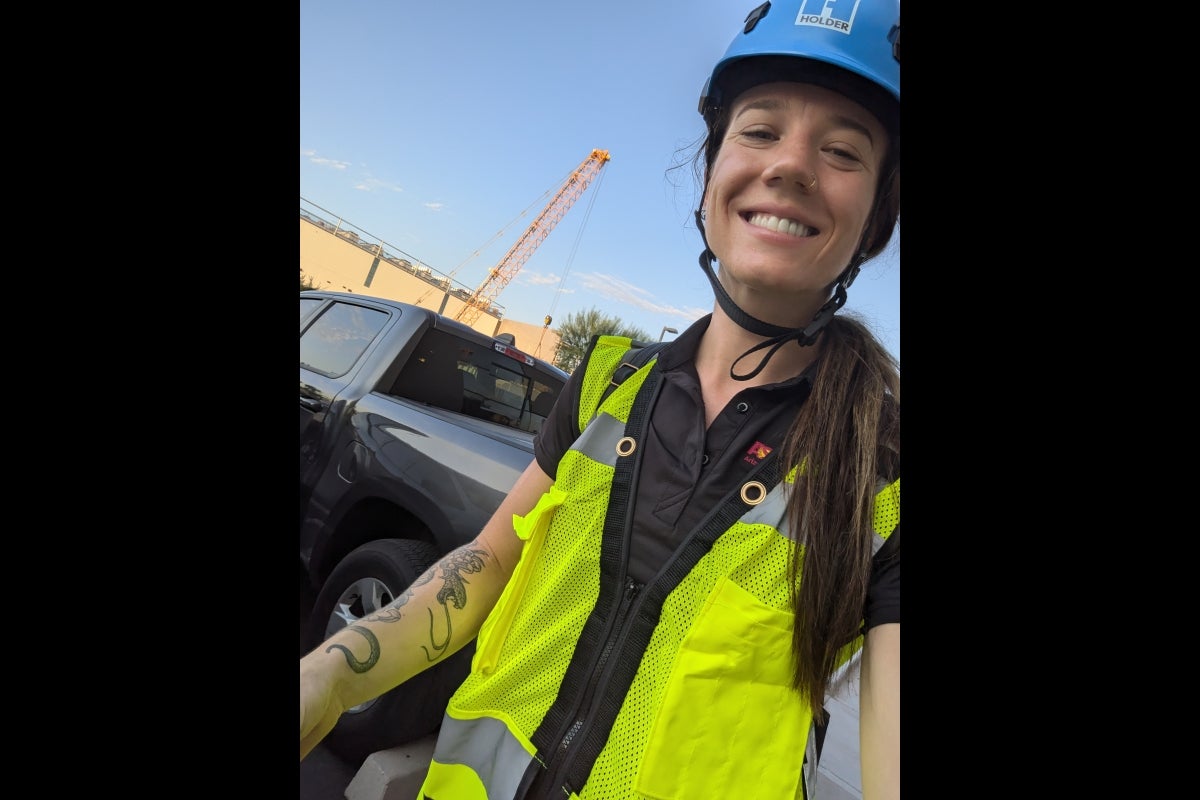 Woman wearing a bright yellow construction vest and blue helmet smiles.