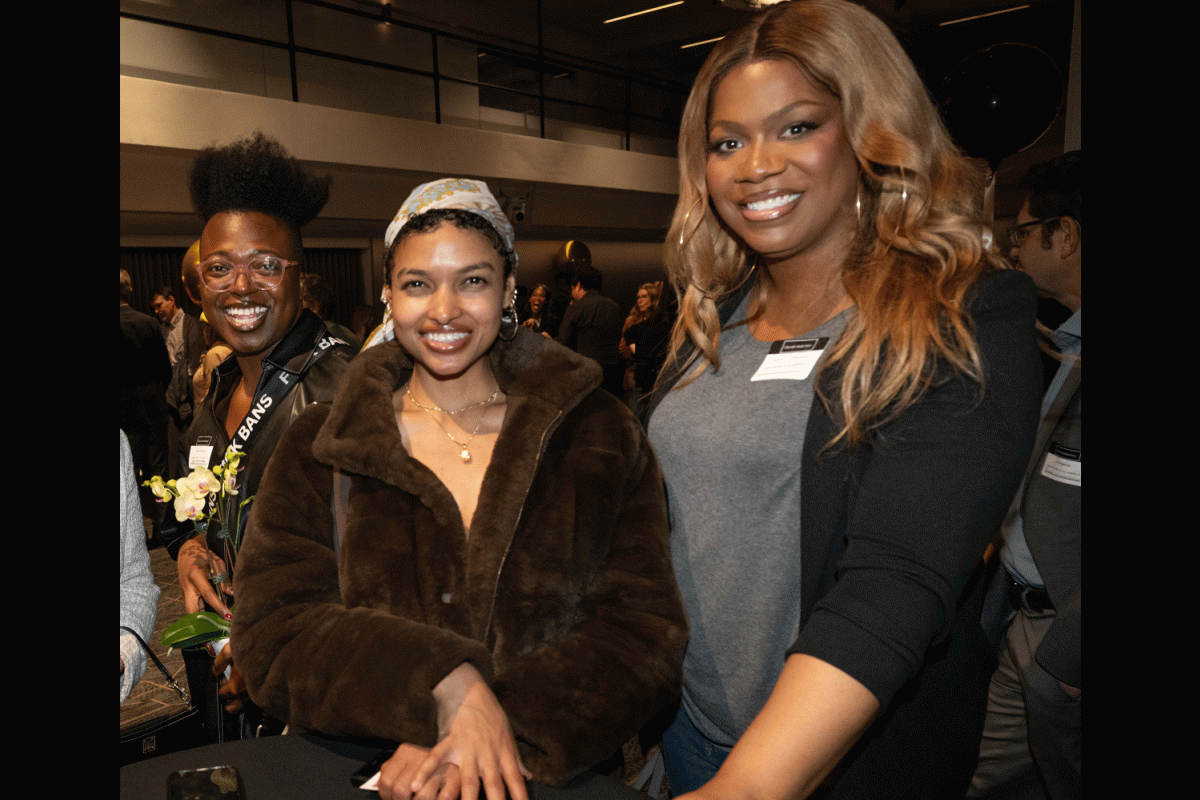 Three women standing at a high-top table smile at the camera